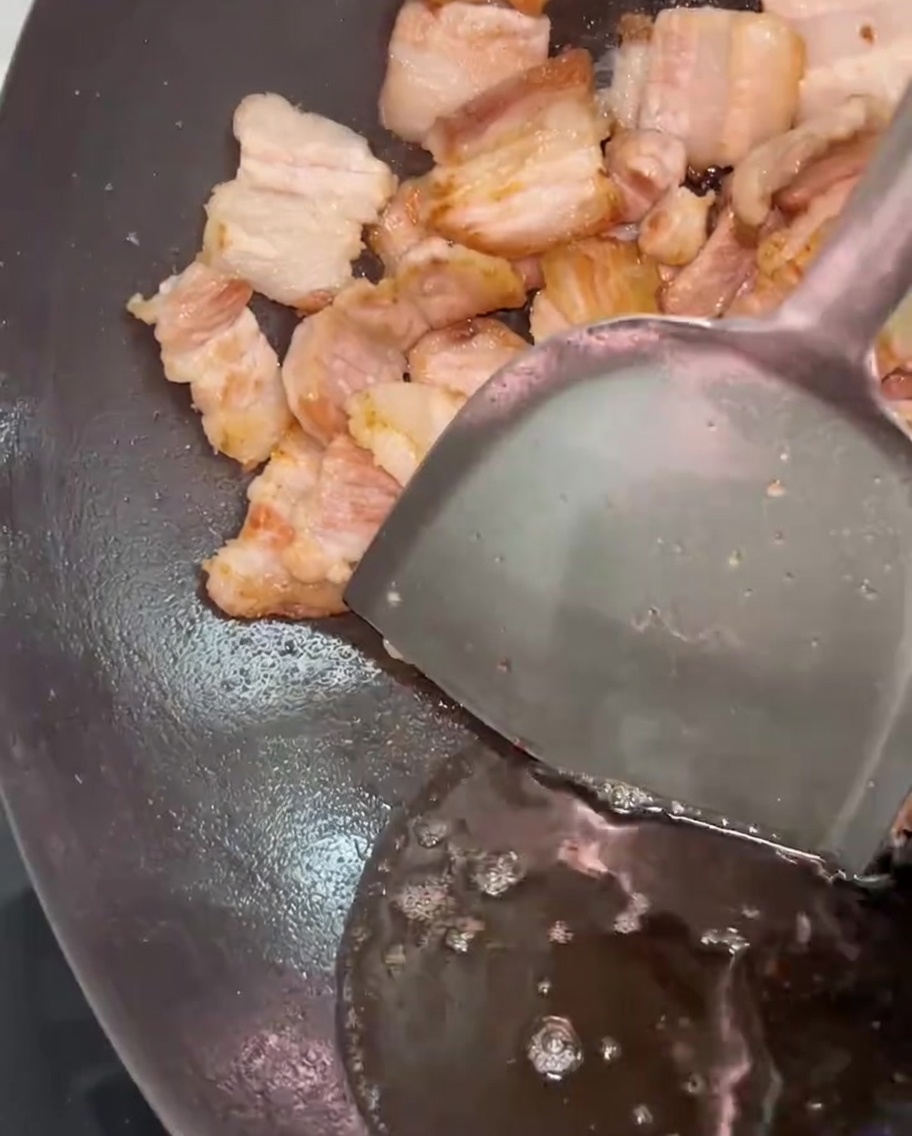 Ein Metallspatel schiebt den Schweinebauch beiseite, während Fett abgegossen wird.