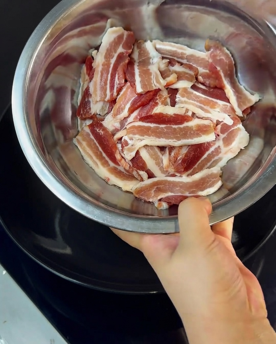 Dünne Schweinebauchscheiben werden in einer Metallschüssel mit Maisstärke bestäubt.