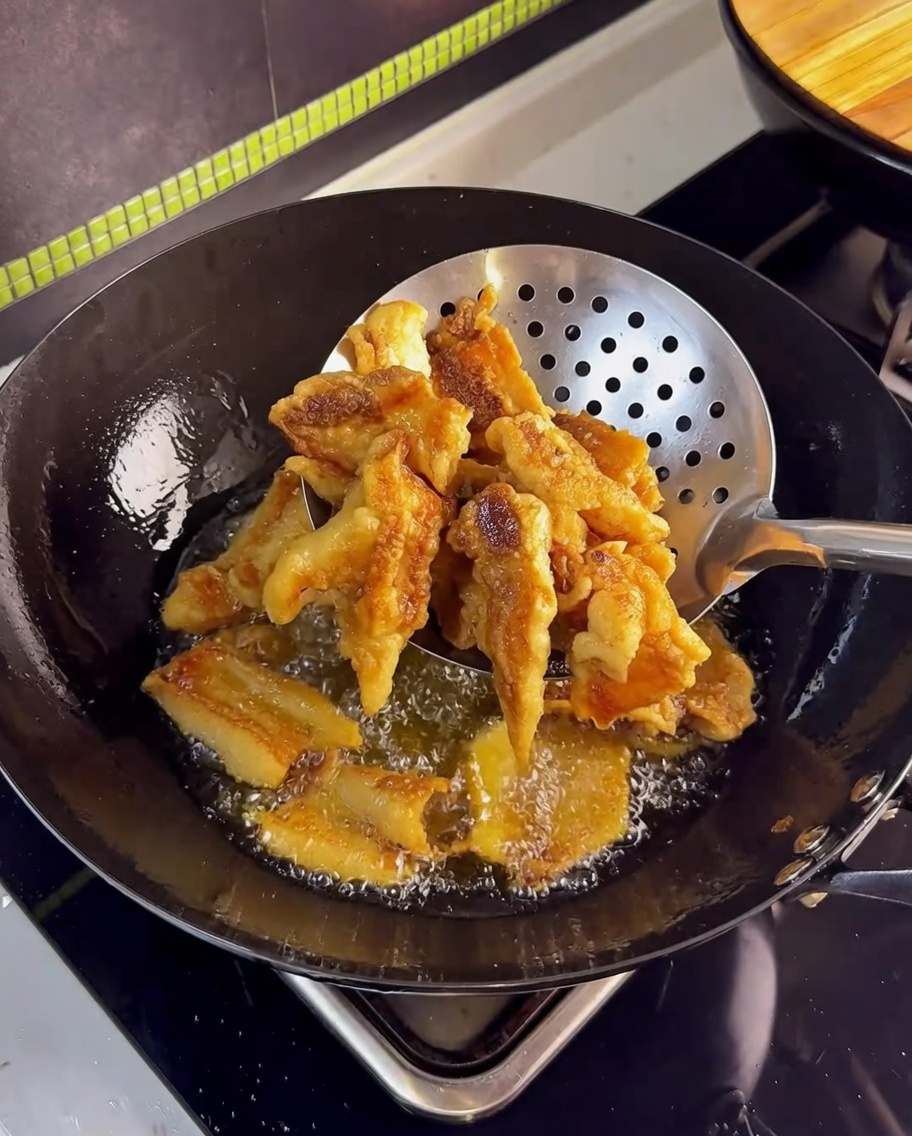 Goldbrauner, knuspriger Schweinebauch wird mit einem Sieb aus dem heißen Öl gehoben.