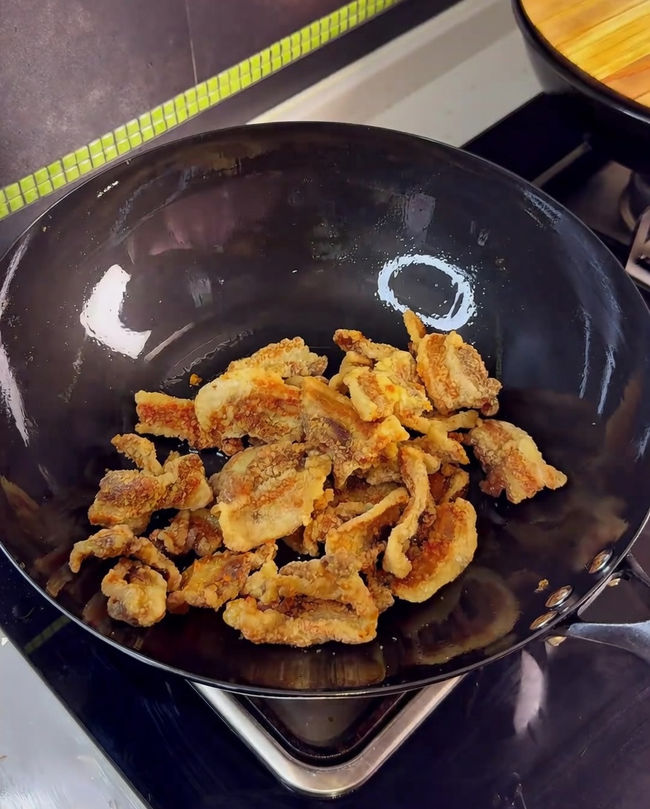 Knusprig frittierte Schweinebauchstücke werden im Wok mit Knoblauch und der Soja-Sauce angebraten.