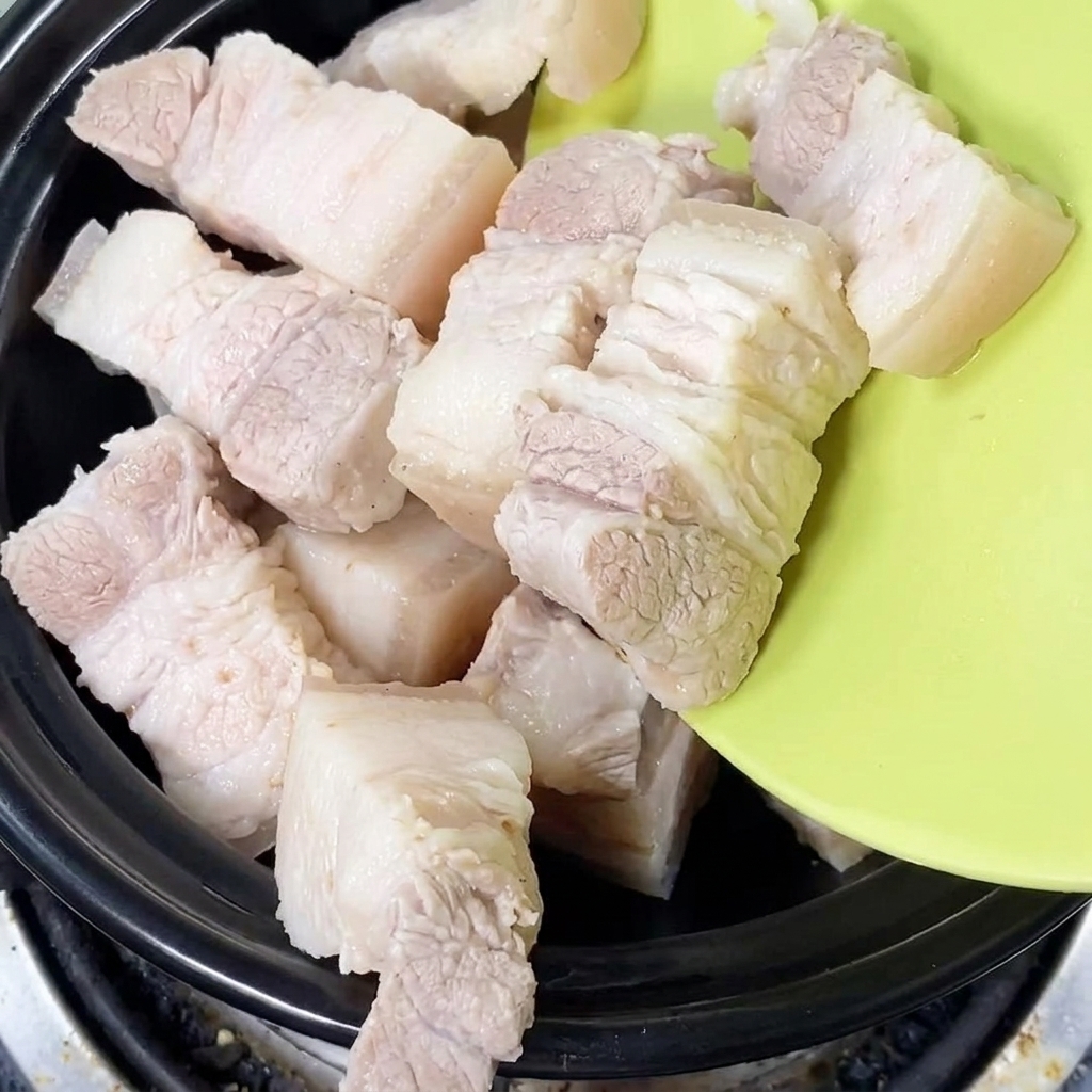 Frisch blanchierte Schweinebauchstücke werden in einen schwarzen Tontopf gelegt.