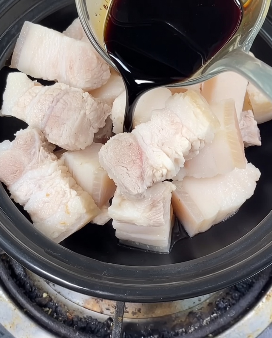 Helle und dunkle Sojasauce werden über den Schweinebauch im Tontopf gegossen, Kandiszucker ist ebenfalls enthalten.