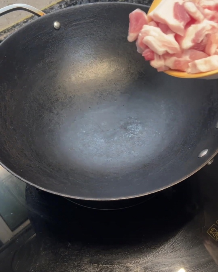 Rohe Schweinebauchscheiben werden in einen heißen, leeren Wok gegeben.