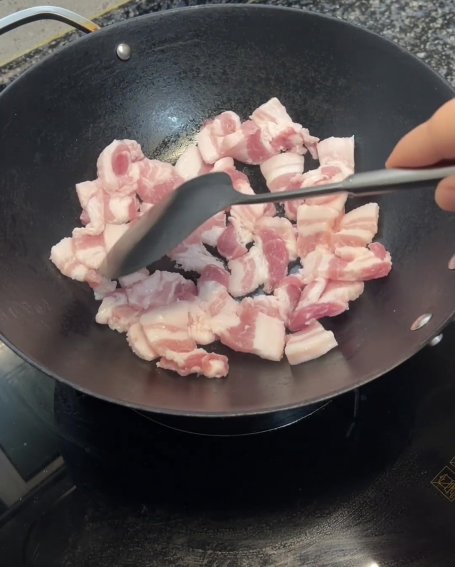 Schweinebauchscheiben werden in einem Wok mit einem Pfannenwender gewendet und zeigen erste Bräunungsspuren.
