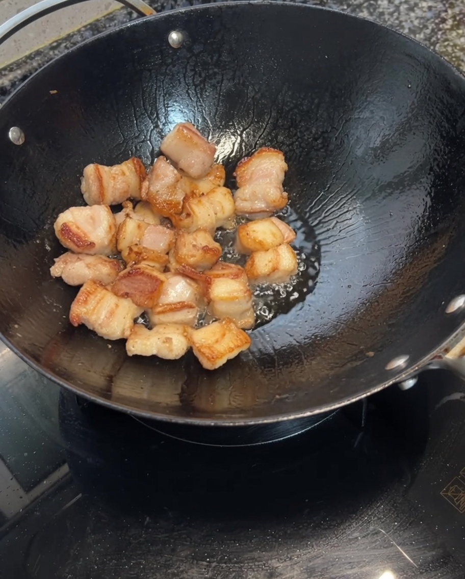 Knoblauchzehen werden zu dem angebratenen Schweinebauch in den Wok gegeben.