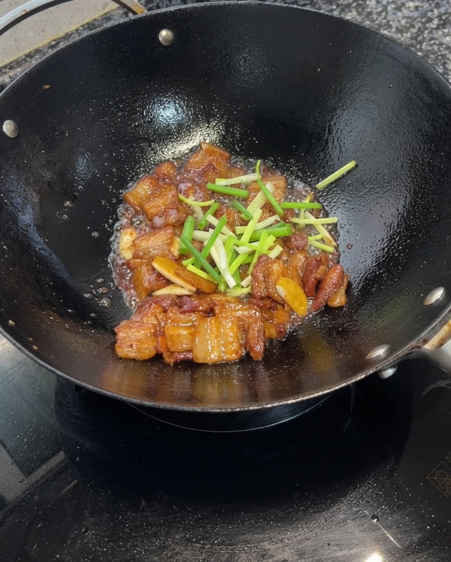 Gehackte Frühlingszwiebeln werden unter den glasierten Schweinebauch im Wok gehoben.
