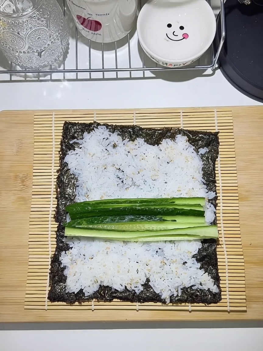 Bambusmatte mit Algenblatt, Reis und belegt mit Gurke, Karotte, Ei und Fleisch.