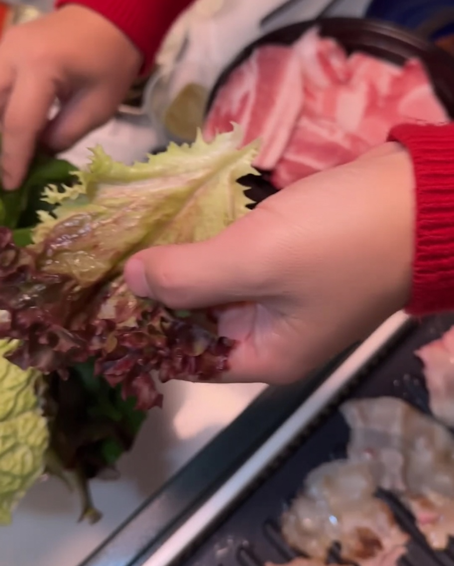Ein Salatblatt wird in einer Hand auf ein Perillablatt gelegt.