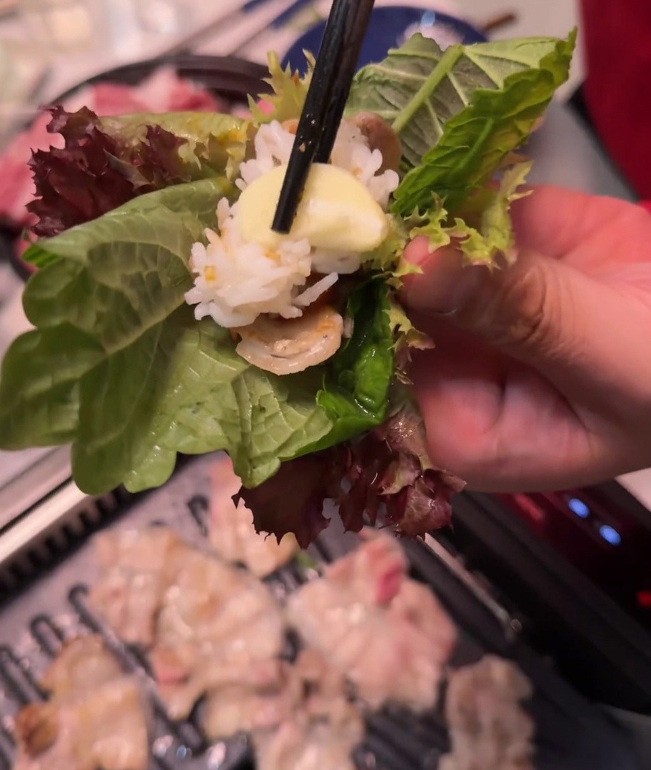 Eine Hand hält einen Salat- und Perillablatt-Wrap mit Fleisch, Reis, Ssamjang und Knoblauch.