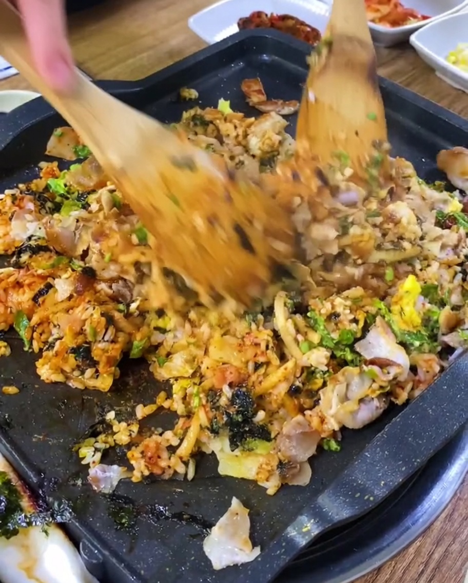 Gebratener Reis mit Fleischstücken auf einem heißen Grill.