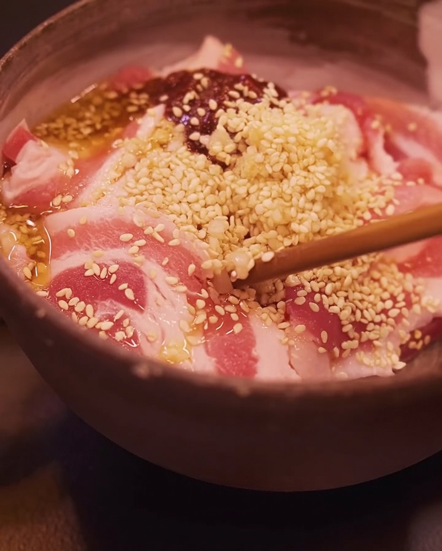 Nahaufnahme von Stäbchen, die den marinierten Schweinebauch in einer Schüssel vermischen.