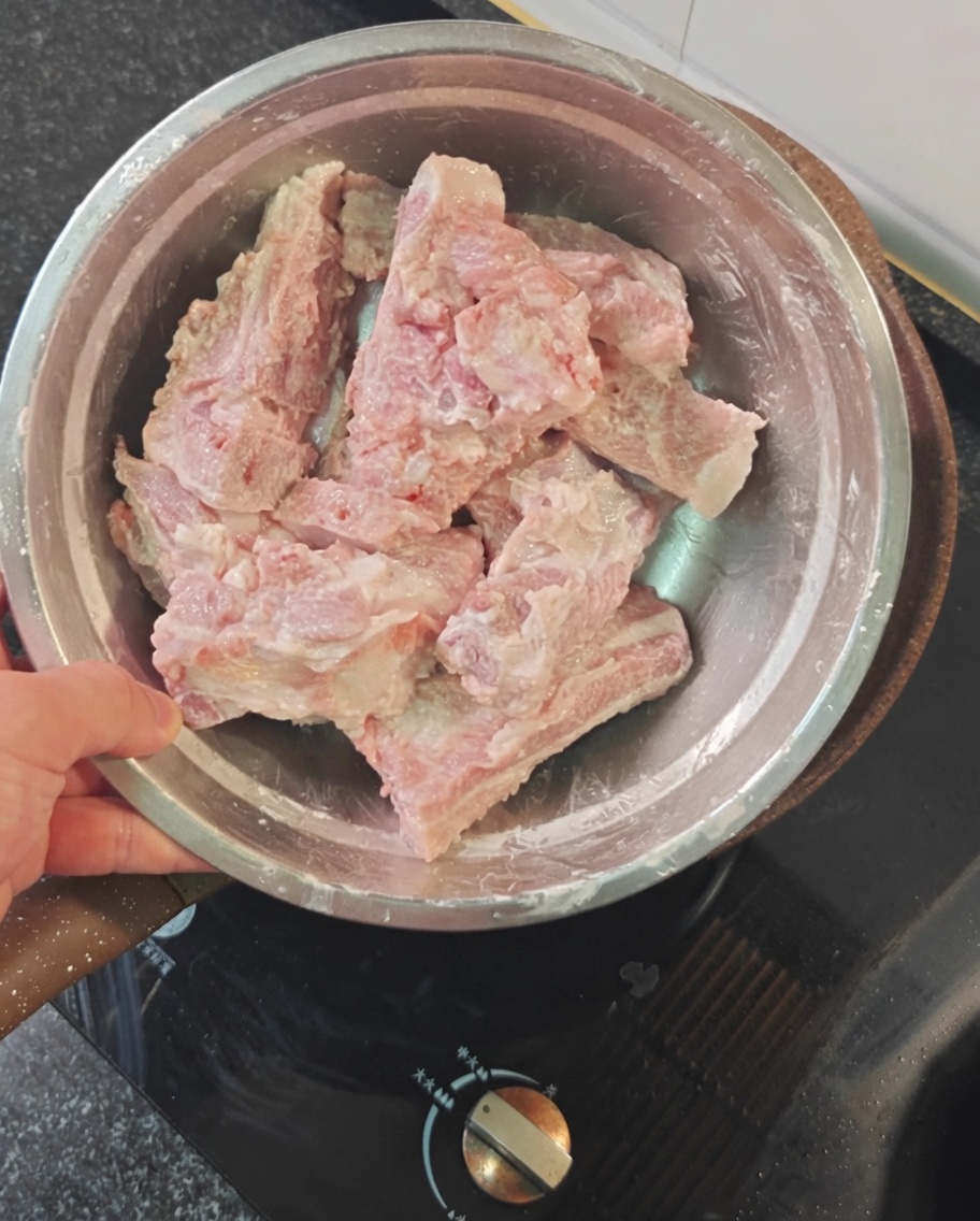 Rohe Schweinerippchen in einer Metallschüssel mit rotem Stärkepulver bestäubt.