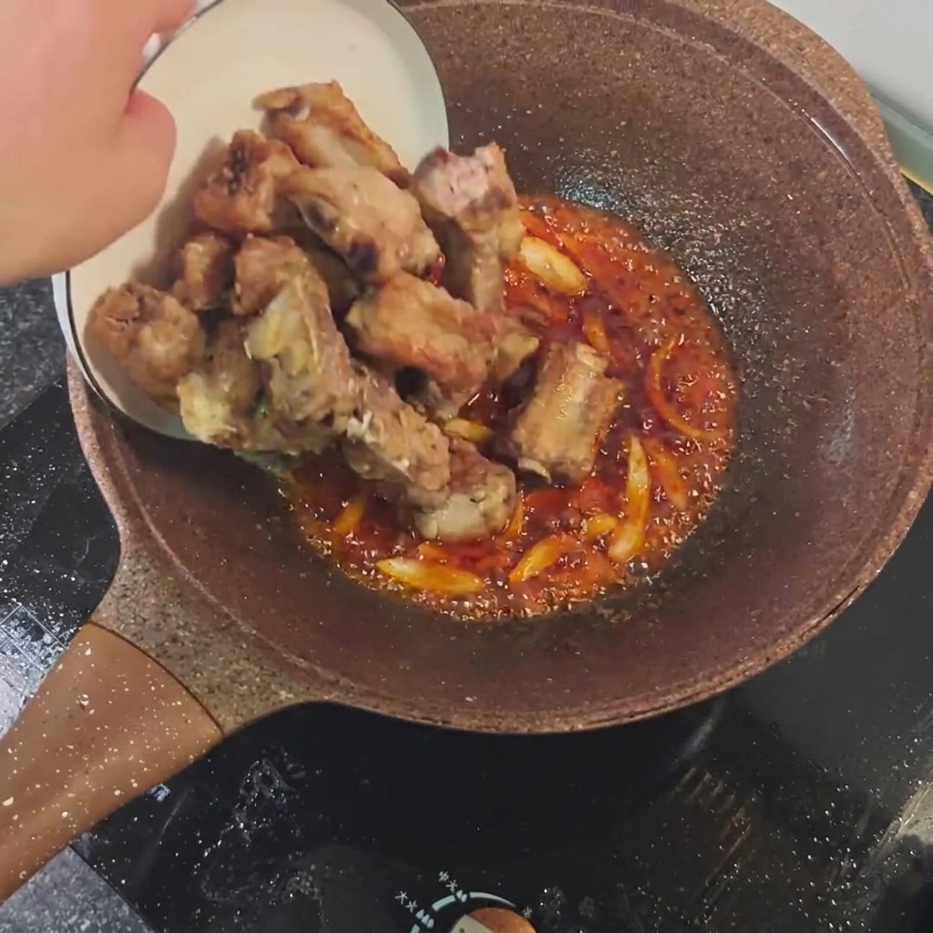 Angebratene Schweinerippchen werden mit der würzigen Sauce und den Aromaten in der Pfanne vermischt.
