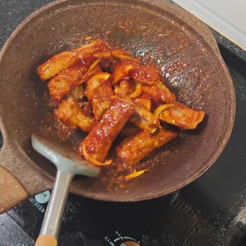 Helle Sojasauce wird über die Schweinerippchen in der Pfanne geträufelt.