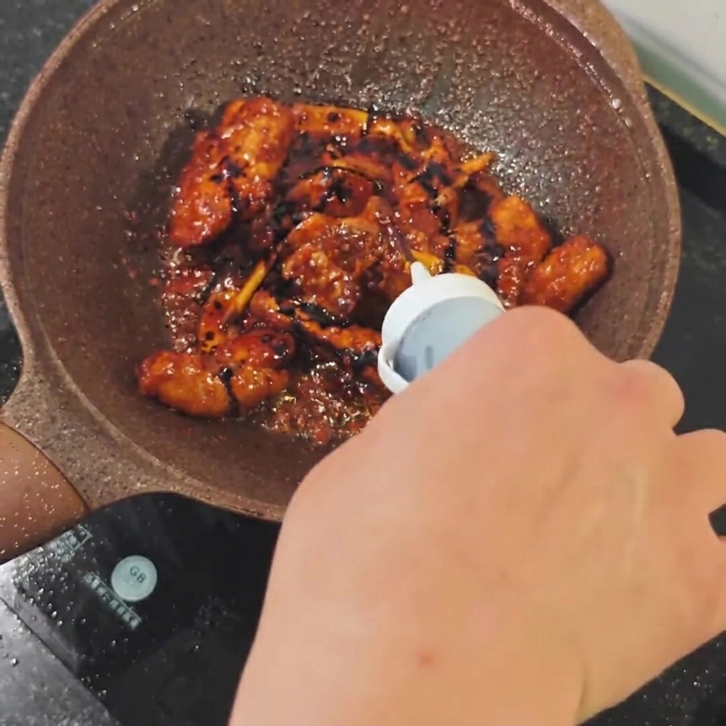 Dunkle Sojasauce wird aus einer kleinen Flasche in eine Pfanne mit anbratenden Schweinerippchen gegossen.