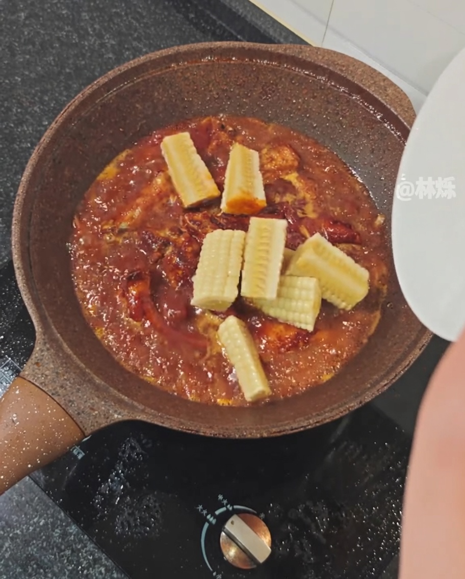 Stücke von frischem Mais werden in eine Pfanne mit schmorenden Schweinerippchen in würziger Sauce gegeben.