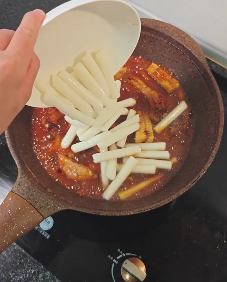 Reiskuchen werden in eine Pfanne mit Schweinerippchen, Mais und würziger Schmorsauce gegeben.