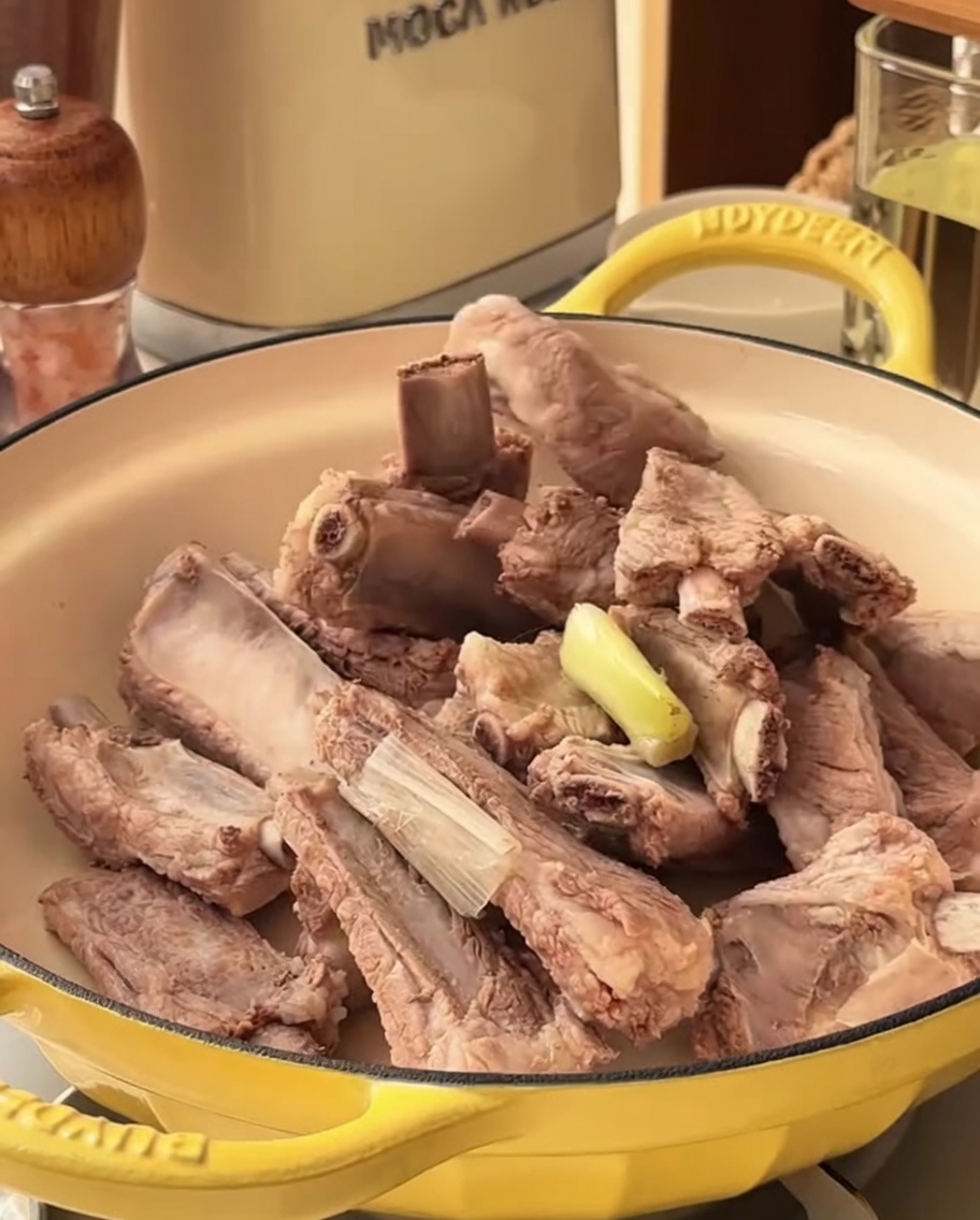Die würzige Marinade wird in einem Topf über die blanchierten Schweinerippchen gegossen.