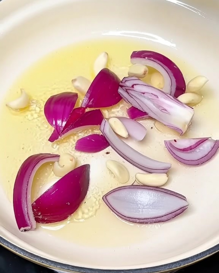 Geschnittene Zwiebeln und Knoblauchzehen werden in heißem Öl in einem Topf angebraten.
