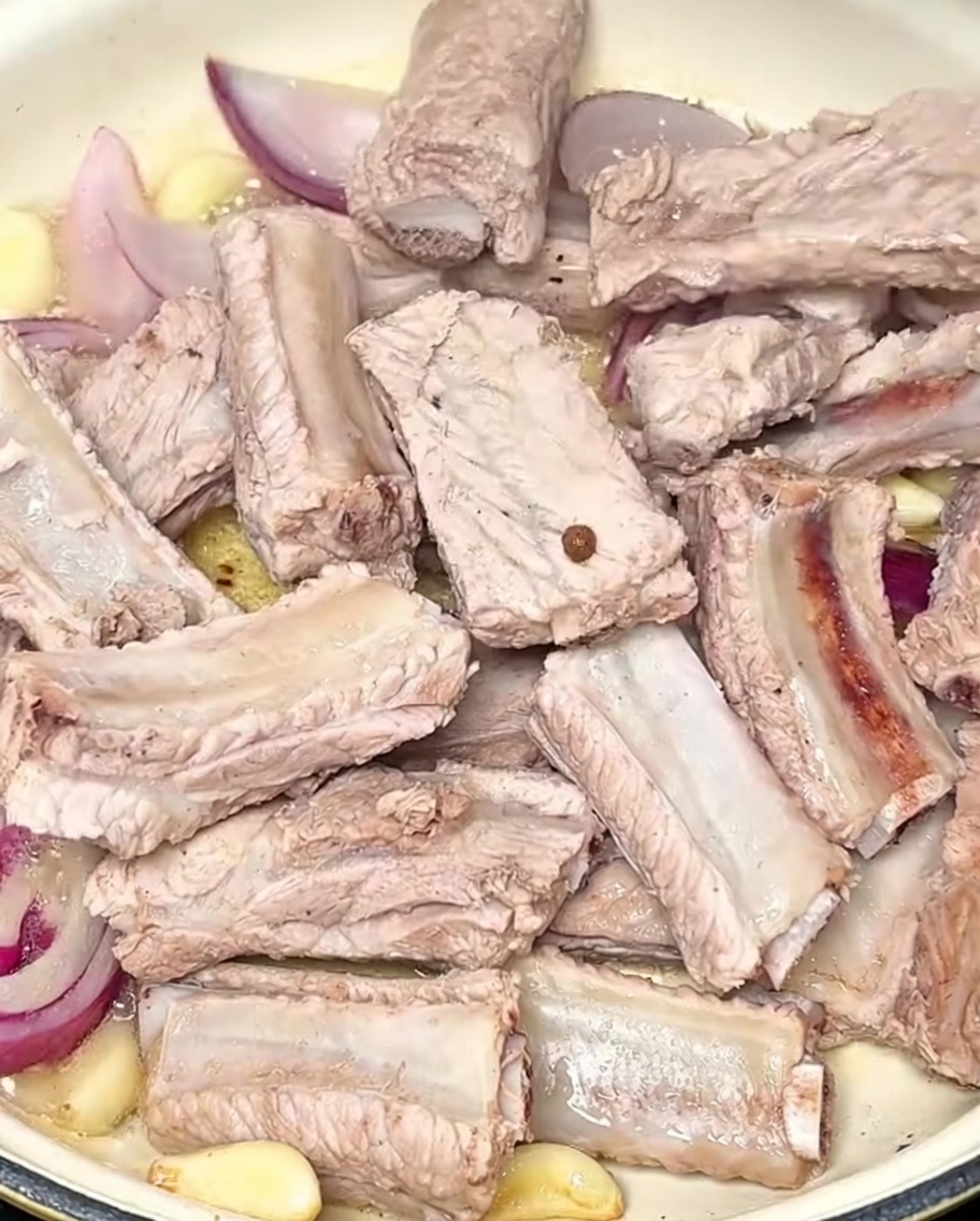 Schweinerippchen werden im Topf zusammen mit Knoblauchzehen und roten Zwiebeln angebraten.