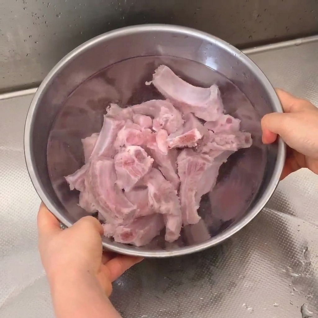 Frische Schweinerippchen, die in einer Edelstahlschüssel unter einem Wasserhahn eingeweicht und abgespült werden.