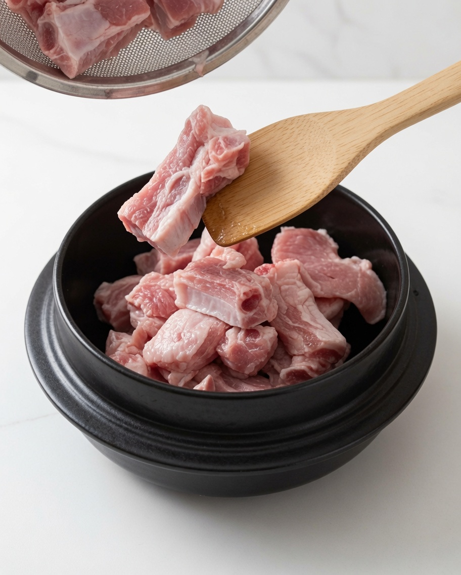 Schweinerippchen werden in einem Topf mit Öl und weißem Zucker unter Verwendung eines Holzlöffels angebraten.