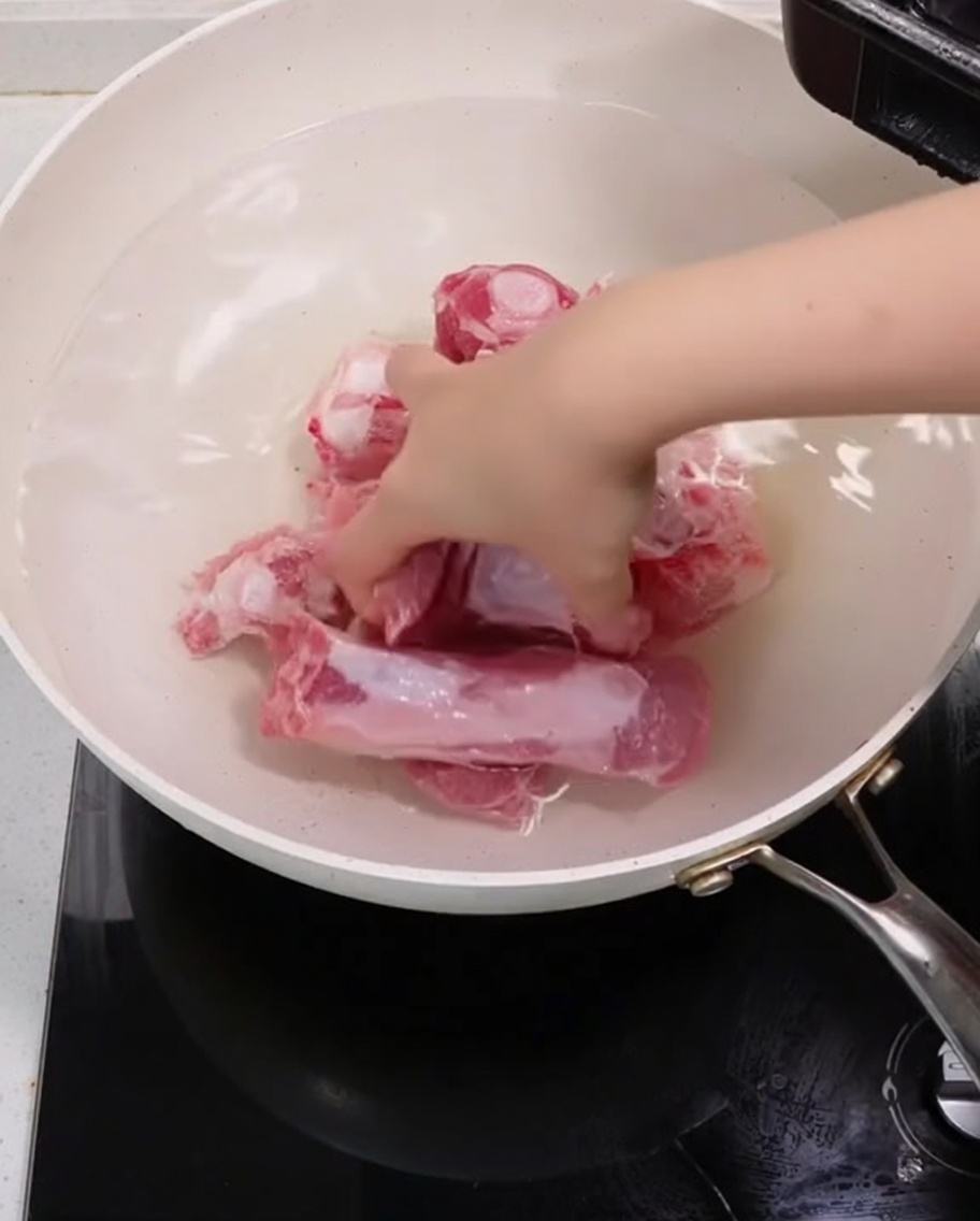 Schweinerippchen kochen in einem Topf mit Frühlingszwiebeln und Ingwerscheiben zum Blanchieren.