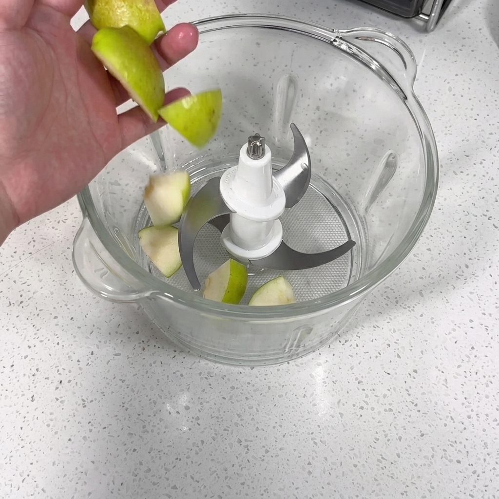Ein Mixer gefüllt mit Stücken von Apfel, Birne, Knoblauch und Zwiebel, die zu einem Püree verarbeitet werden.