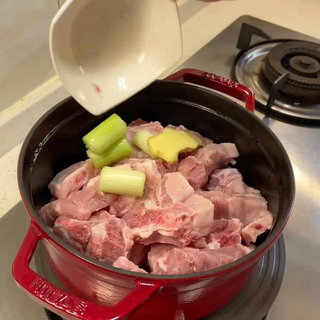 Topf gefüllt mit rohen Schweinerippchen, Ingwer und Frühlingszwiebel bereit zum Kochen.