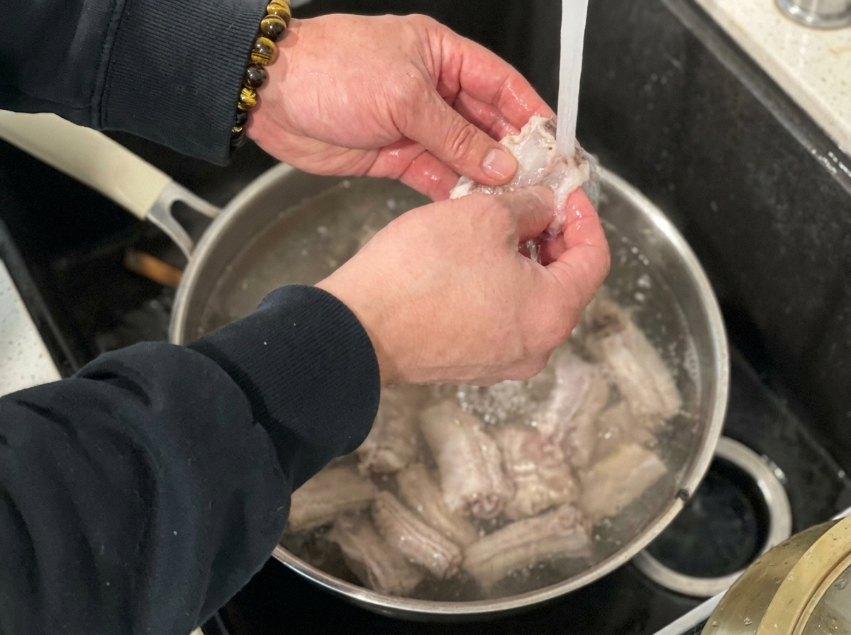 Blanchierte Schweinerippchen werden unter dem Wasserhahn mit fließendem Wasser abgespült.
