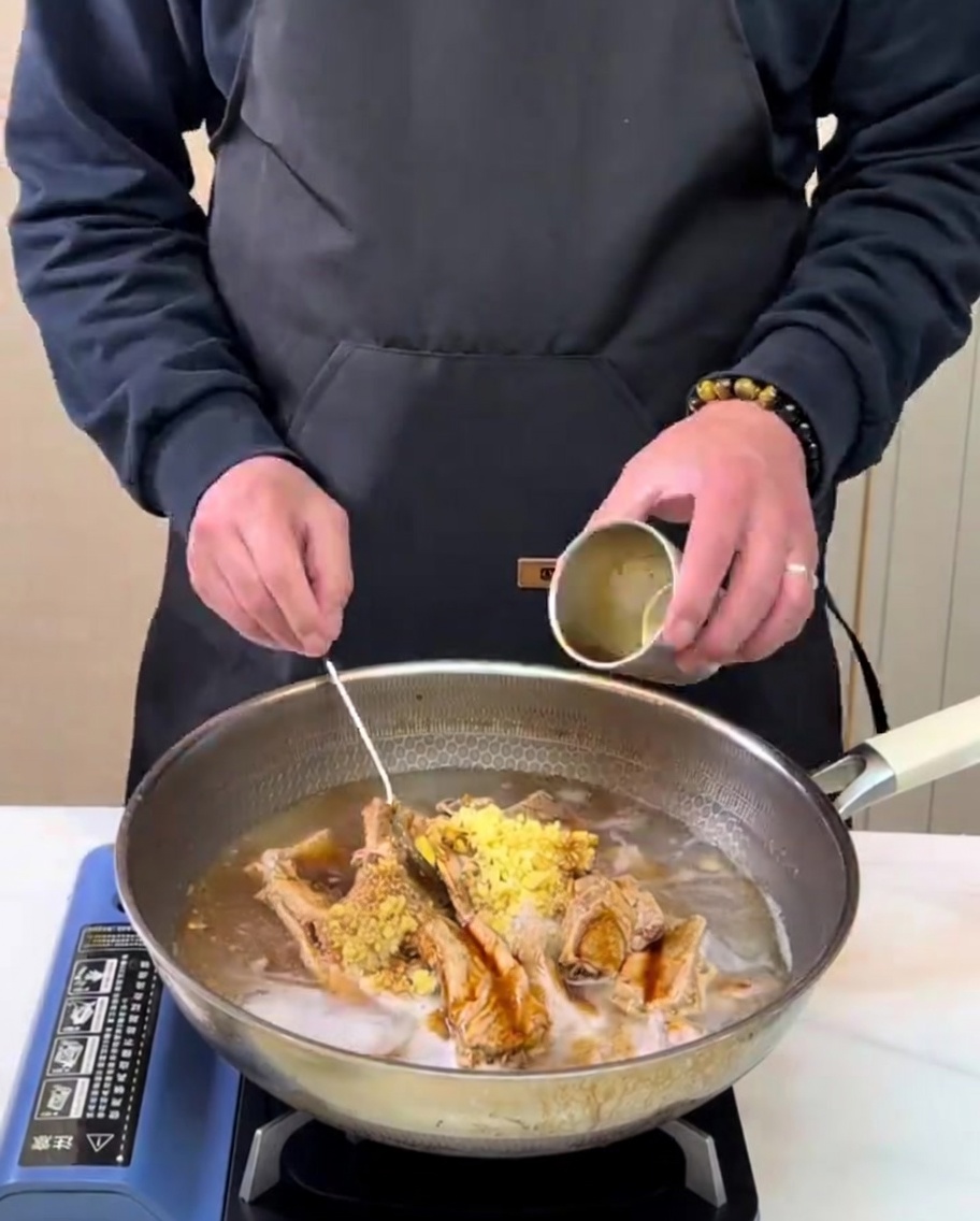 Frisch zubereiteter Birnensaft wird aus einem kleinen Metallbecher in einen Kochtopf mit Rippchen und Gewürzen gegossen.