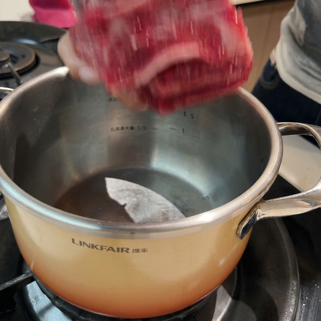 Rinderrippchen in einem Topf mit kaltem Wasser und Gewürzen, bereit zum Blanchieren.