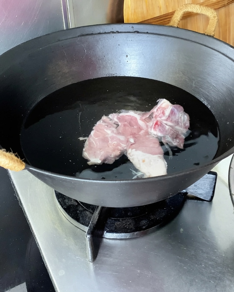 Schweinerücken in einem Wok mit kaltem Wasser, Ingwer, Frühlingszwiebeln und Kochwein.