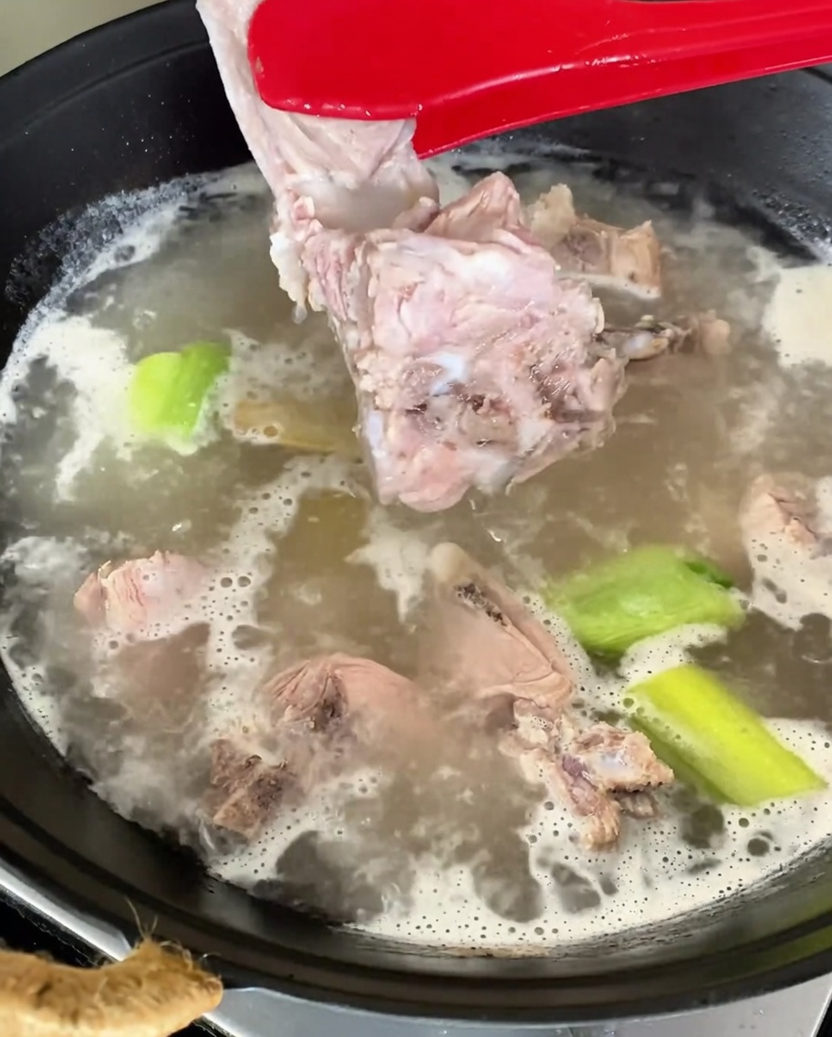 Blanchierte Schweinerückenstücke werden mit einer roten Zange aus dem kochenden Wasser gehoben.