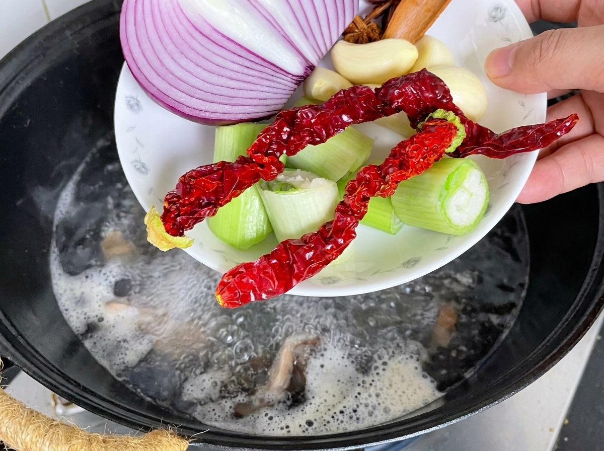 Schweinerücken im Wok mit Aromaten, während kochendes Wasser hinzugegossen wird.