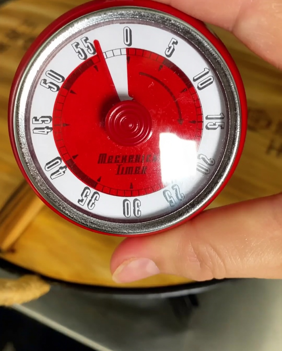 Ein Küchentimer auf eine Stunde eingestellt, im Hintergrund ein köchelnder Topf.