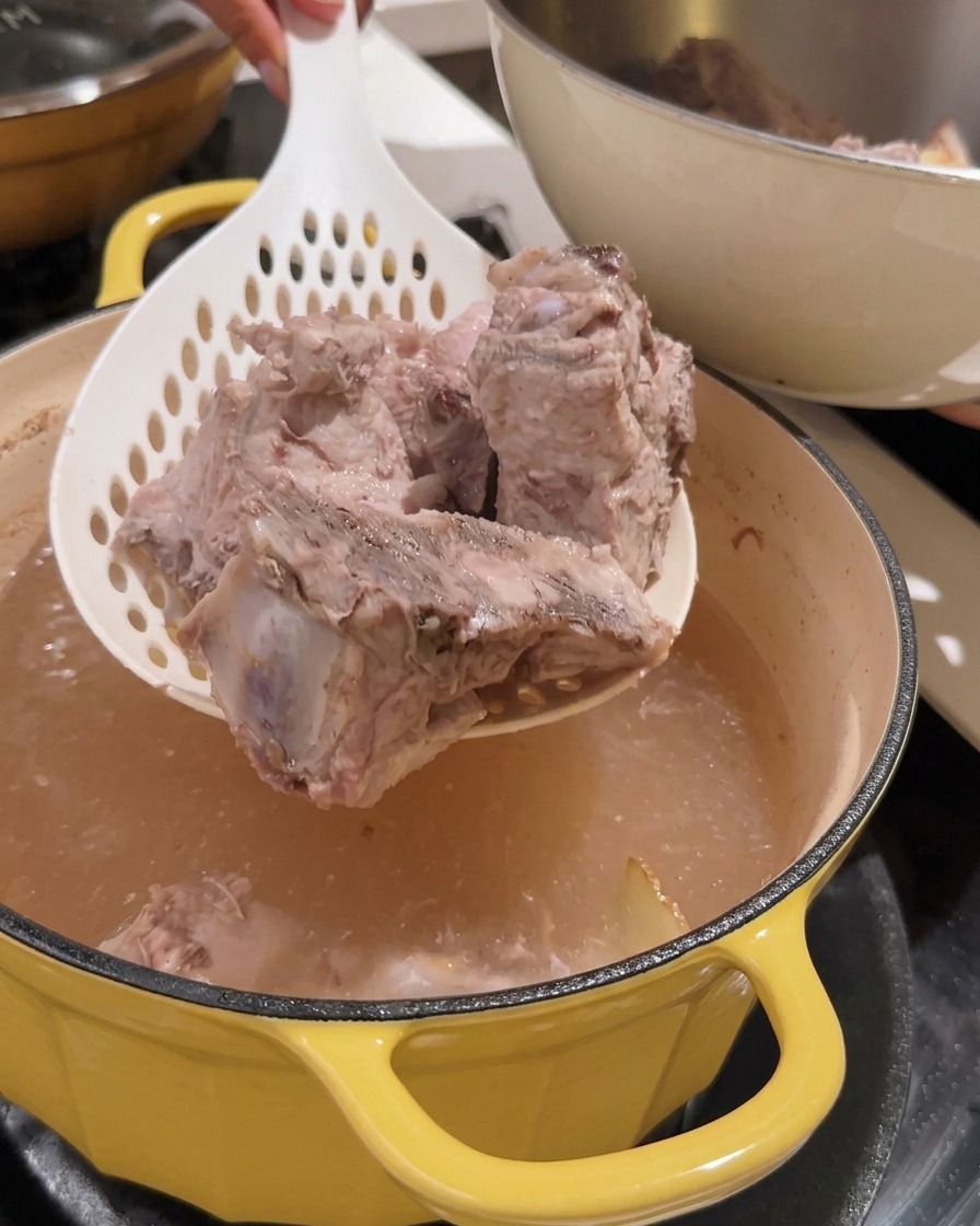 Sieb hebt blanchierte Rippchenstücke aus dem Topf.
