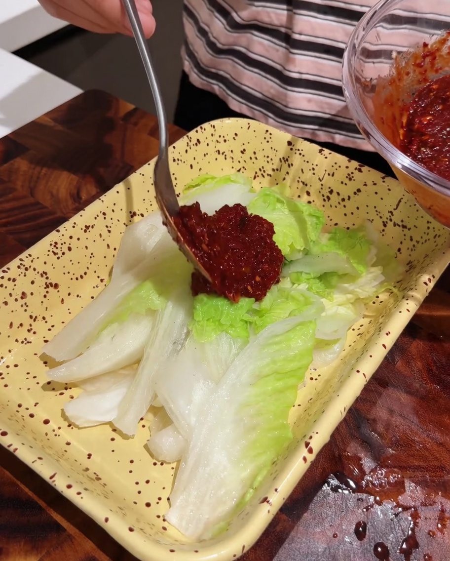 Ein Löffel verteilt rote Würzpaste auf Kohlblättern.