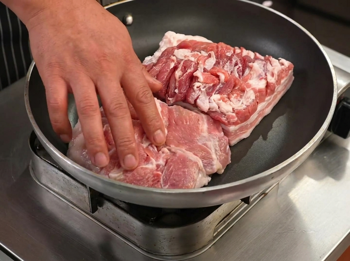 Schweinebauchscheiben braten in einer trockenen Pfanne und beginnen, ihr Fett auszulassen.