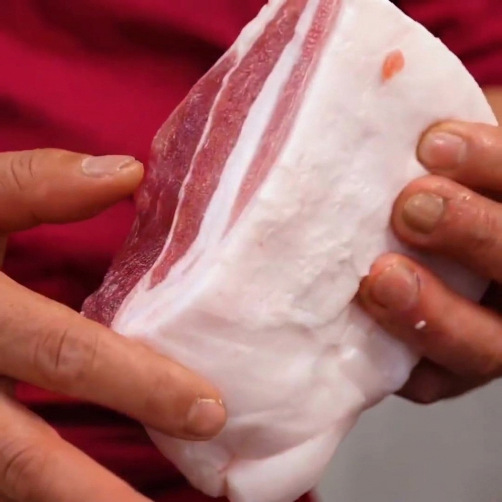 Schweinebauch in den Händen gehalten, zeigt die im 45-Grad-Winkel gemachten Rauten Schnitte.