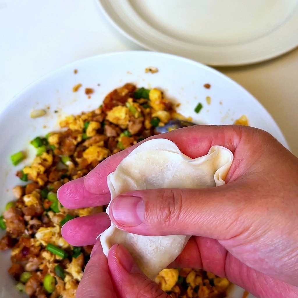 Eine Hand hält ein mit der Barbecue-Fleischmischung gefülltes Teigblatt und faltet es zusammen.