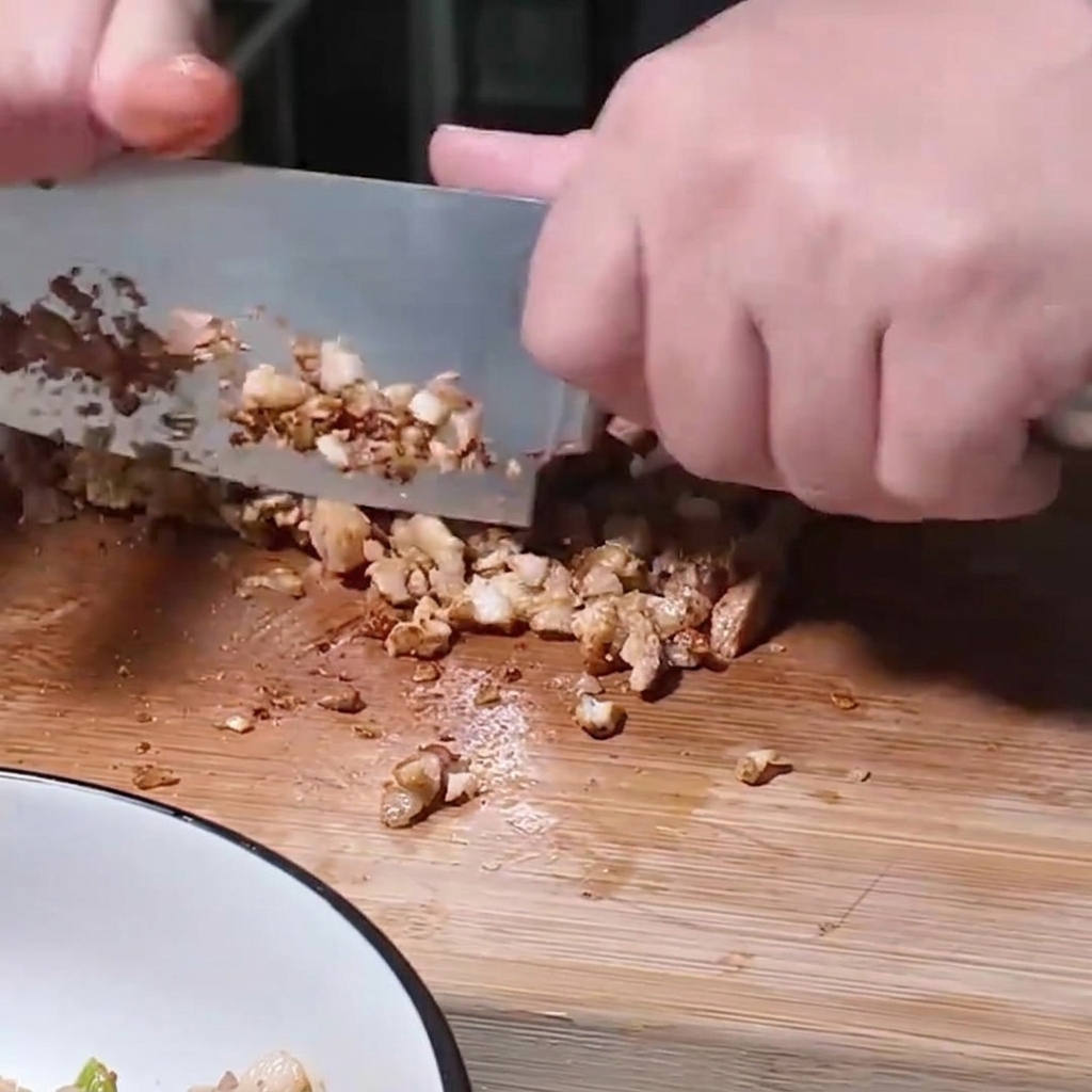Jemand hackt mit einem großen Messer gegartes Schweinefleisch auf einem Holzbrett.