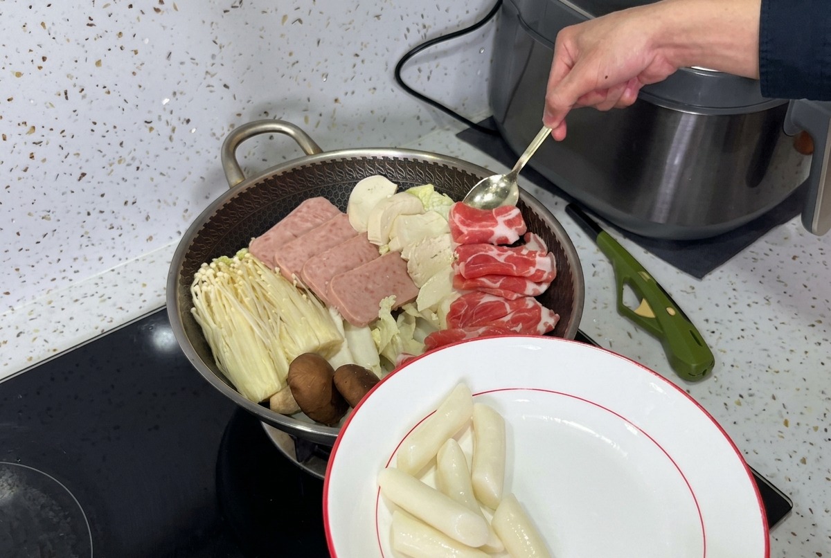 Ein wunderschoen angerichteter Topf mit Koreanischem Armeeeintopf mit Lagen aus Fleischangebot, Pilzen, Tofu und frischem Kimchi, bereit fuer die Bruehe.