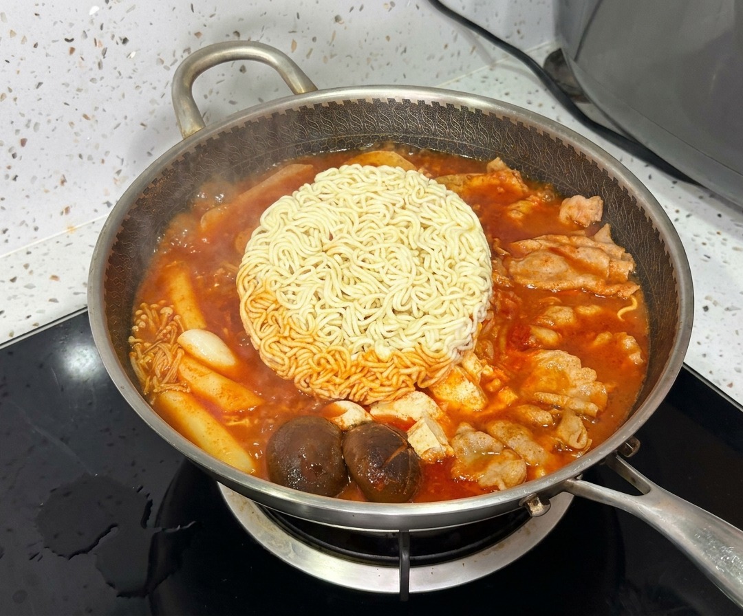 Ein Block Ramennudeln kocht in der Mitte des lebhaften, blubbernden koreanischen Armeeeintopfs.