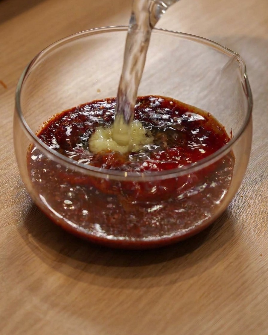 Wasser wird in eine Glasschüssel mit Chilipulver und Gewürzen gegossen.