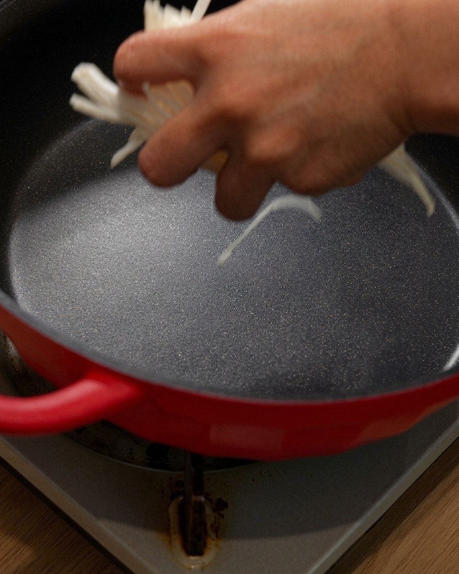 Frisch geschnittene Zwiebelstreifen werden auf den Boden eines roten Topfes gegeben.