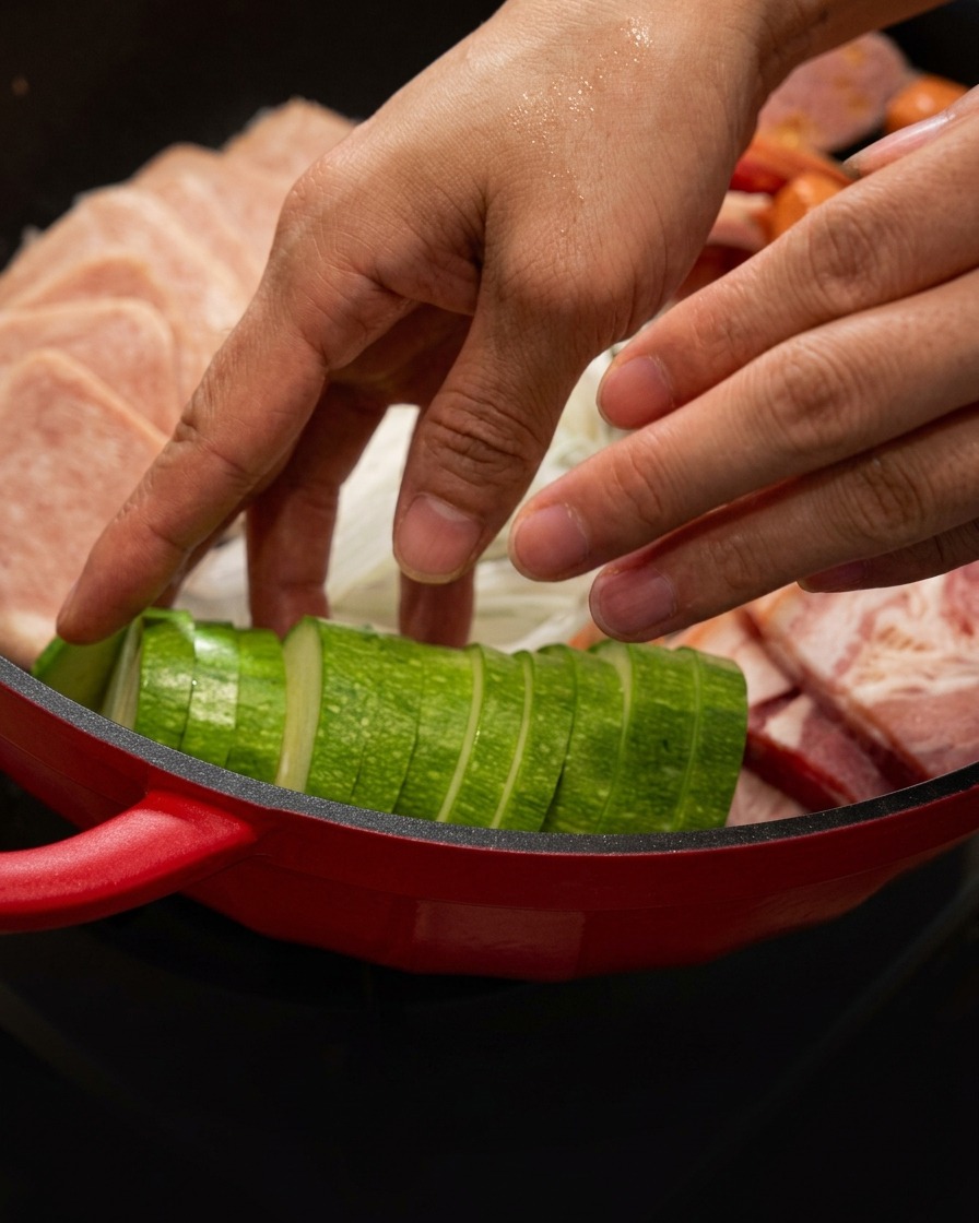 Zucchinischnitze werden säuberlich neben dem Fleisch in den roten Topf gelegt.
