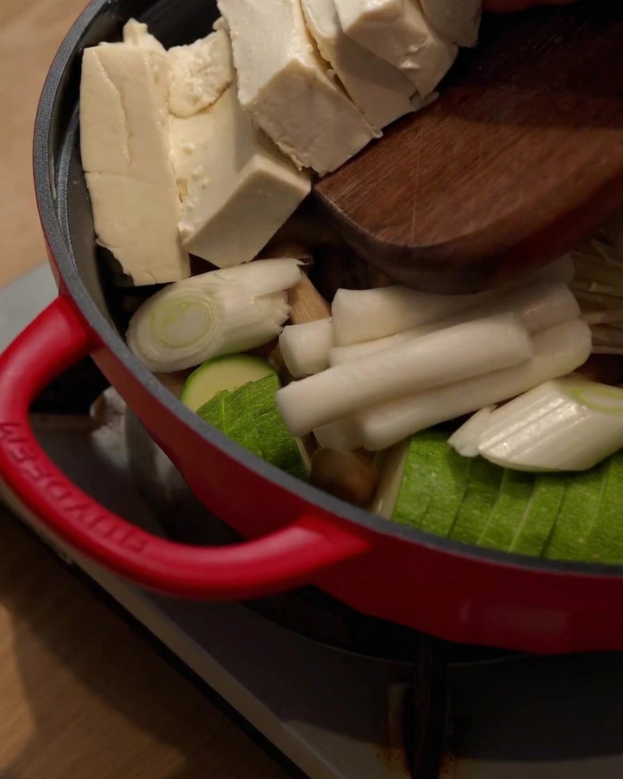 Tofublöcke werden von einem Holzschneidebrett in den Hot Pot mit den anderen Zutaten geschoben.