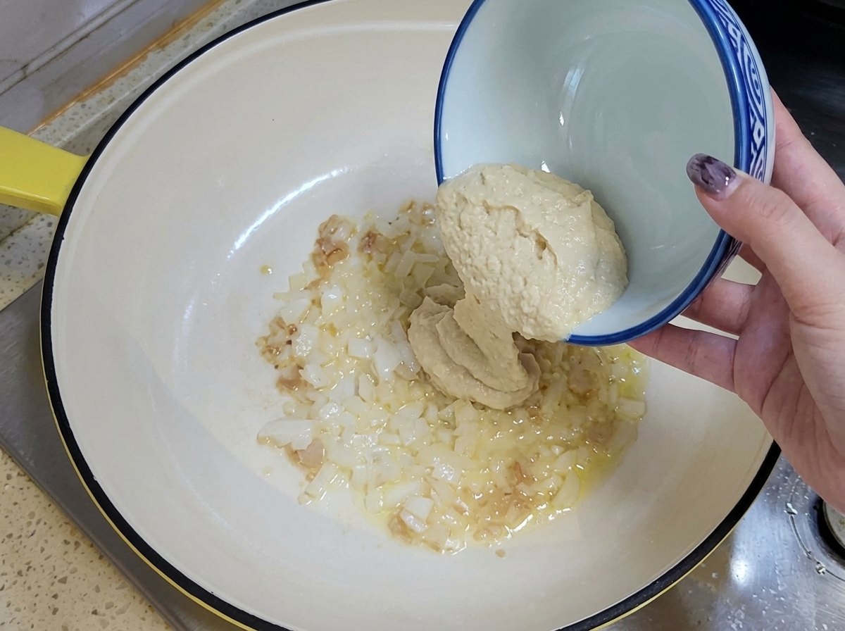 Gehackter Knoblauch und gewürfelte Zwiebeln werden aus einer Keramikschüssel in eine geölte Pfanne gegeben.