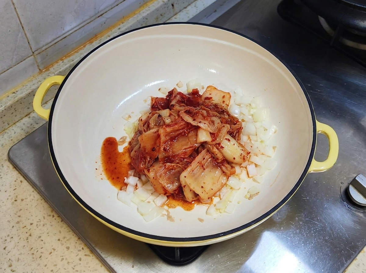 Eine Portion roter fermentierter Kimchi liegt auf angebratenen Zwiebeln in einer weißen Pfanne.
